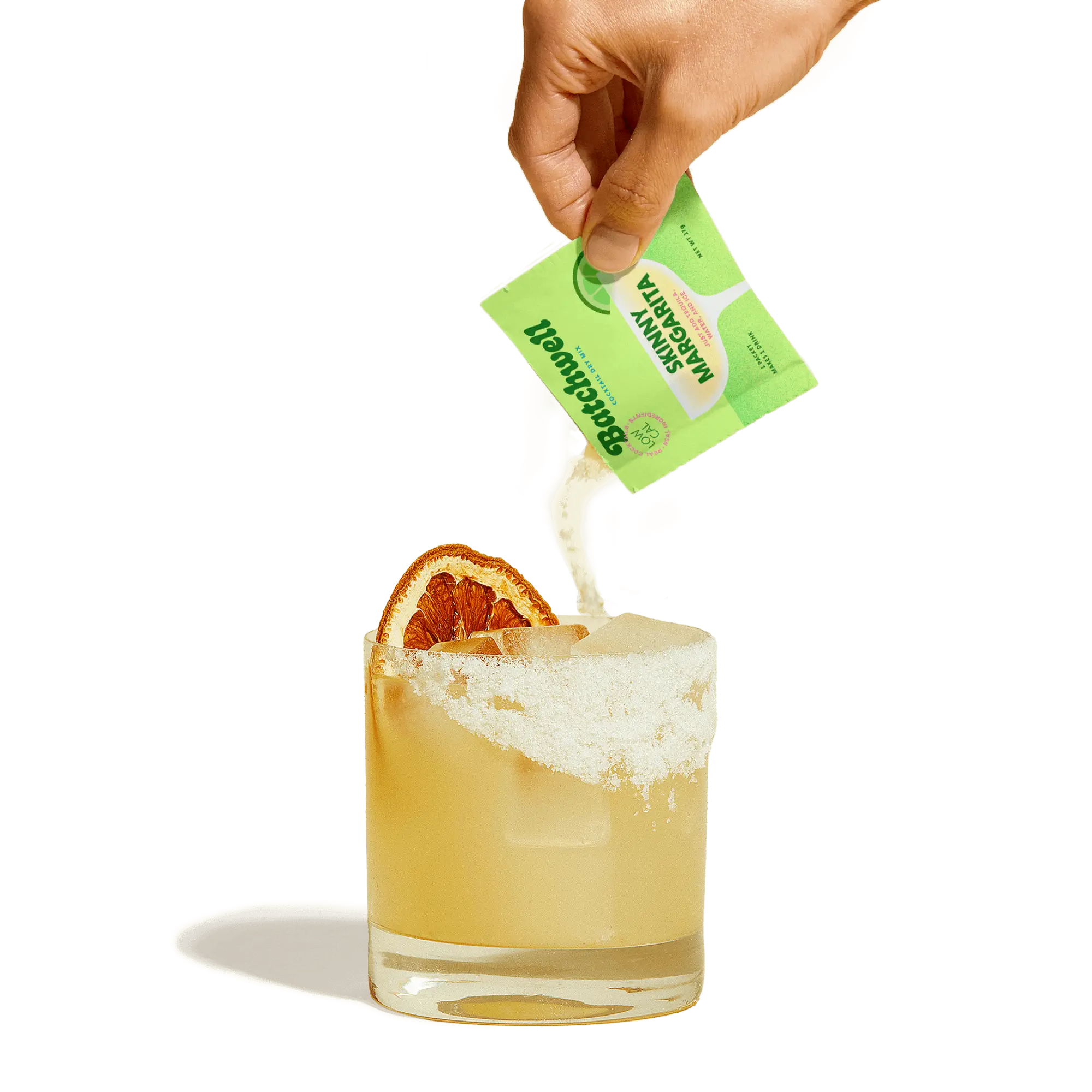 hand pouring a skinny margarita sachet into a glass with ice, a salted rim, and a dried lime on top